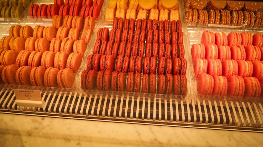 Assorted colorful French macarons in Parisian patisserie display, priced at 1.50€ each.