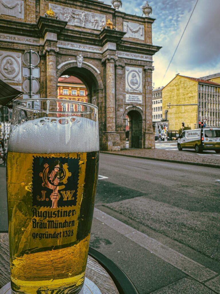 A glass of Augustiner Bräu München beer with the historic Triumphforte of Innsbruck in the background.
