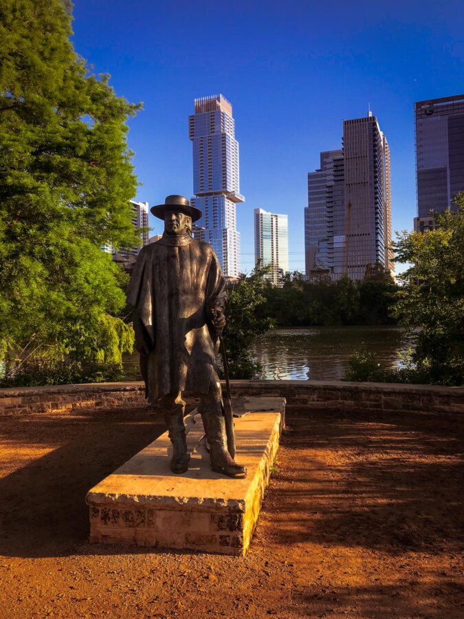 Historic bronze statue before Austin skyline at dusk