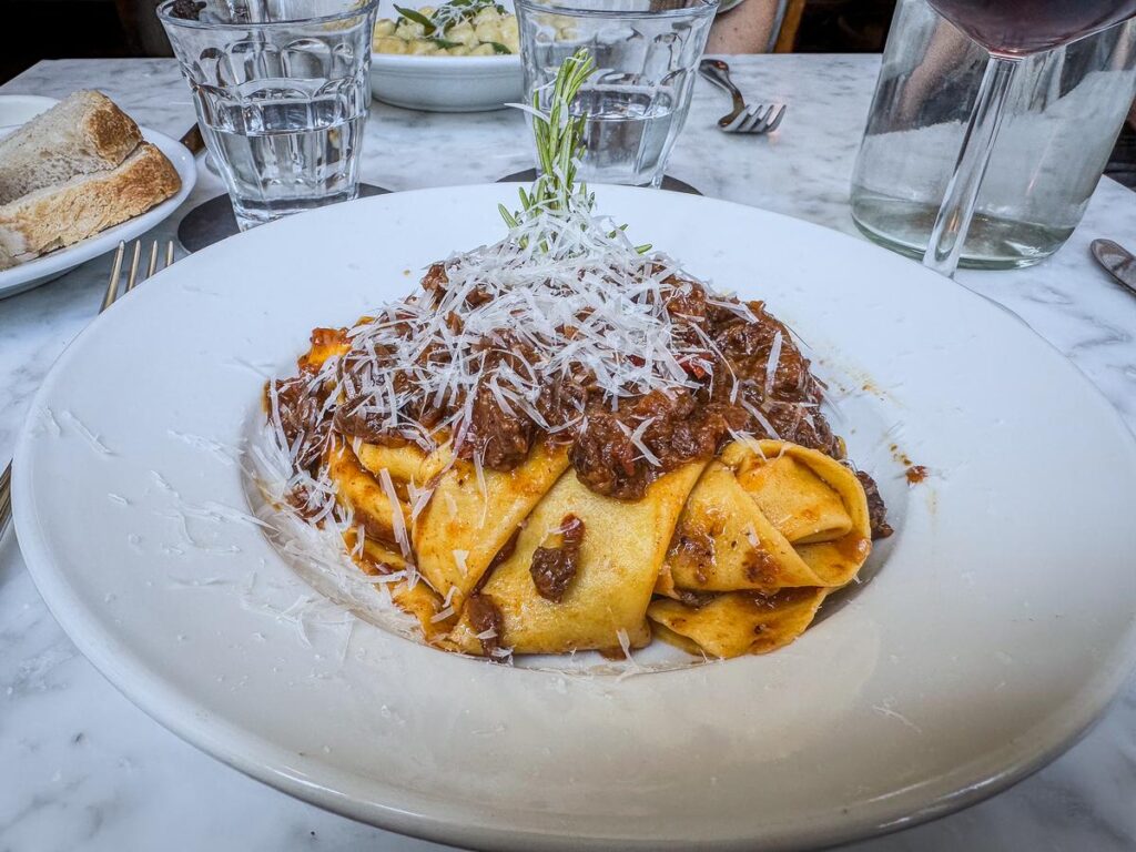 Plate of freshly made bolognese pasta with Parmesan, water, and wine in Amsterdam restaurant.