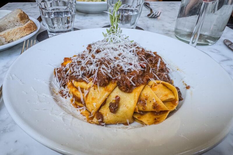 Plate of freshly made bolognese pasta with Parmesan, water, and wine in Amsterdam restaurant.