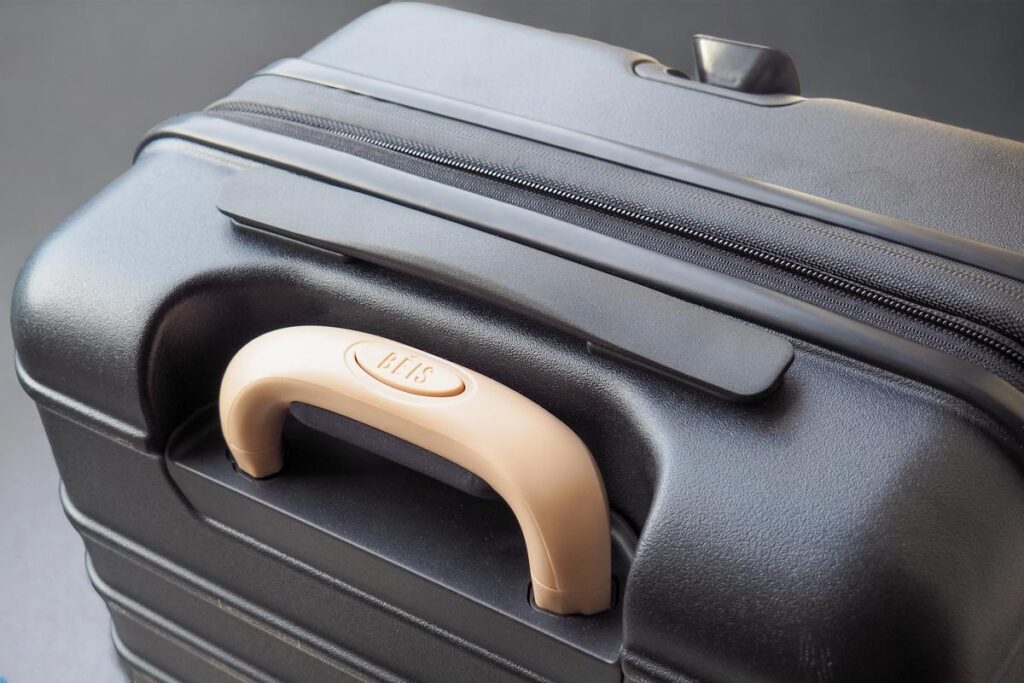 Close-up of Beis carry-on roller handle and zipper, showcasing elegant black textured hard shell and brand's signature detail.