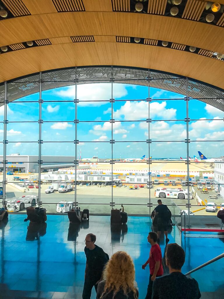 Inside view of Charles De Gaulle Airport terminal with passengers and airplanes, reflecting the lively Parisian atmosphere.