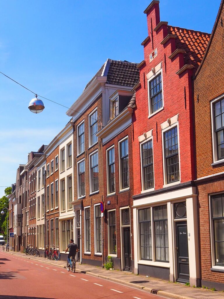 Charming street scene in Leiden with traditional Dutch architecture, red and brick facades, and a bicyclist.