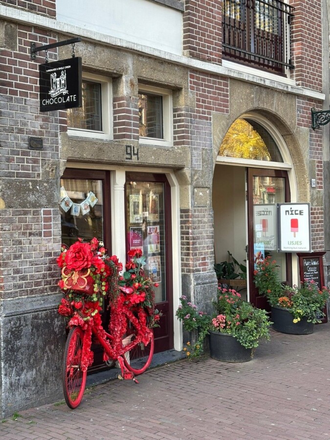 Chocolate shop among shops in Amsterdam with red flower bicycle.
