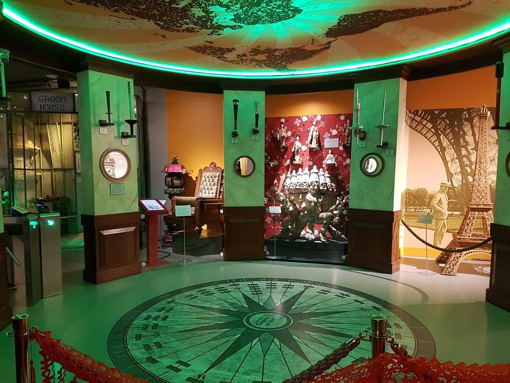 Theater-like exhibition space with a compass-floor centerpiece, green LED ring, alcove displays, and historic scenes.