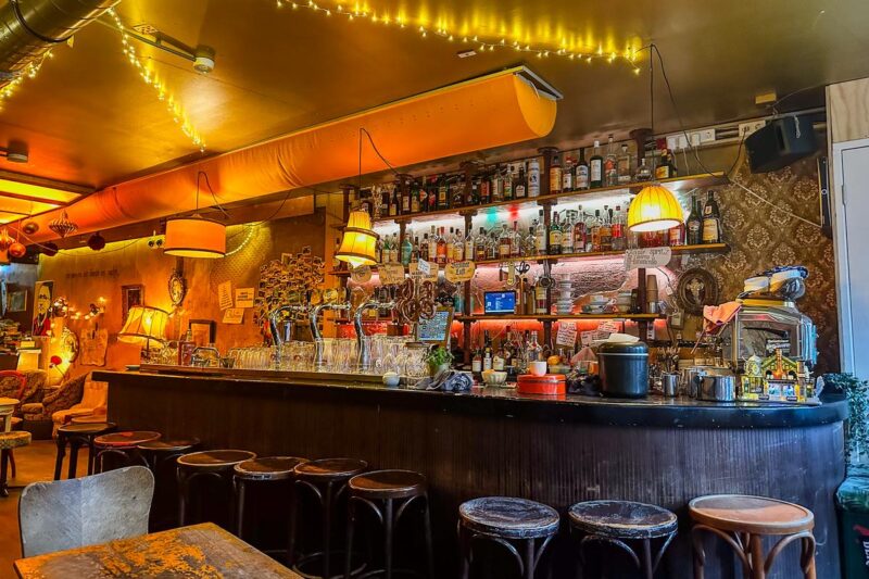 Interior view of cozy Berlin-style café in Amsterdam with bar, string lights, and vintage furniture.
