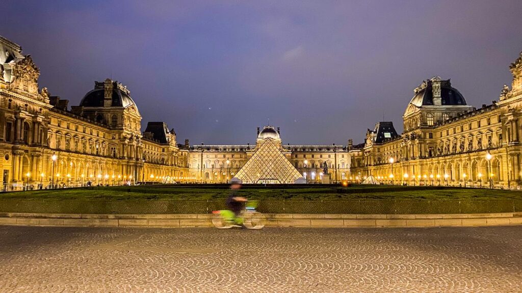Cyclist passing illuminated Louvre Pyramid at dusk in Paris