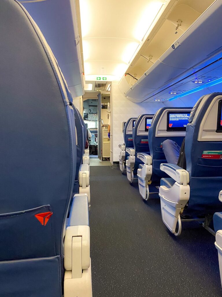 First-class cabin interior on Delta Air Lines with blue leather seats and the airline's logo visible, reflecting the upscale ambiance on a domestic flight.