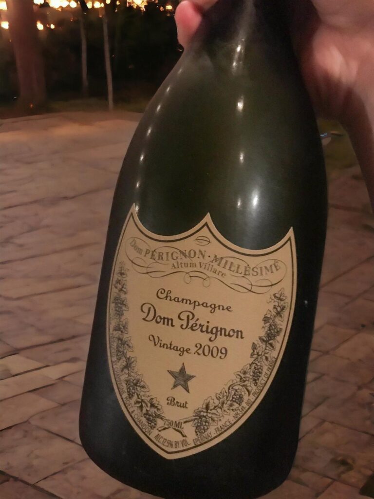 Hand holding Dom Perignon Vintage 2009 Champagne bottle amidst blurred lights, exuding luxury and celebration.