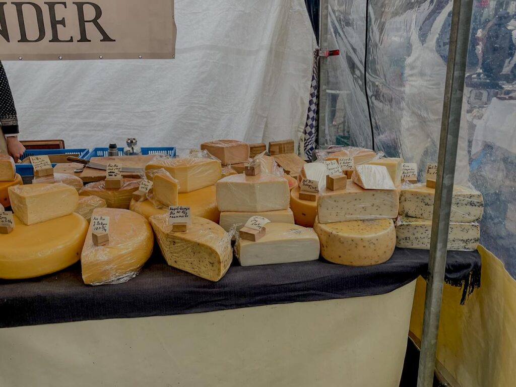Assorted Dutch cheese display at Albert Cuyp Market with vendor in background.