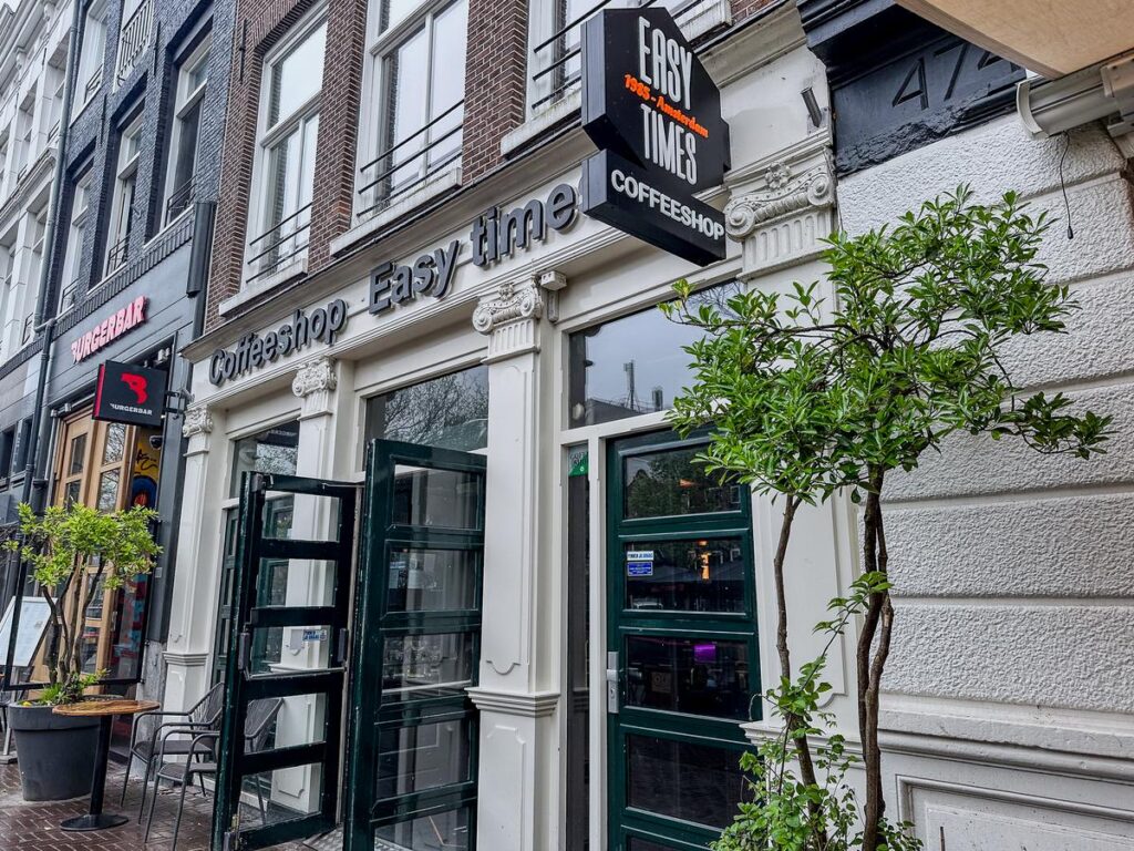 Exterior view of Easy Times Coffeeshop in Amsterdam with glass doors and potted tree.
