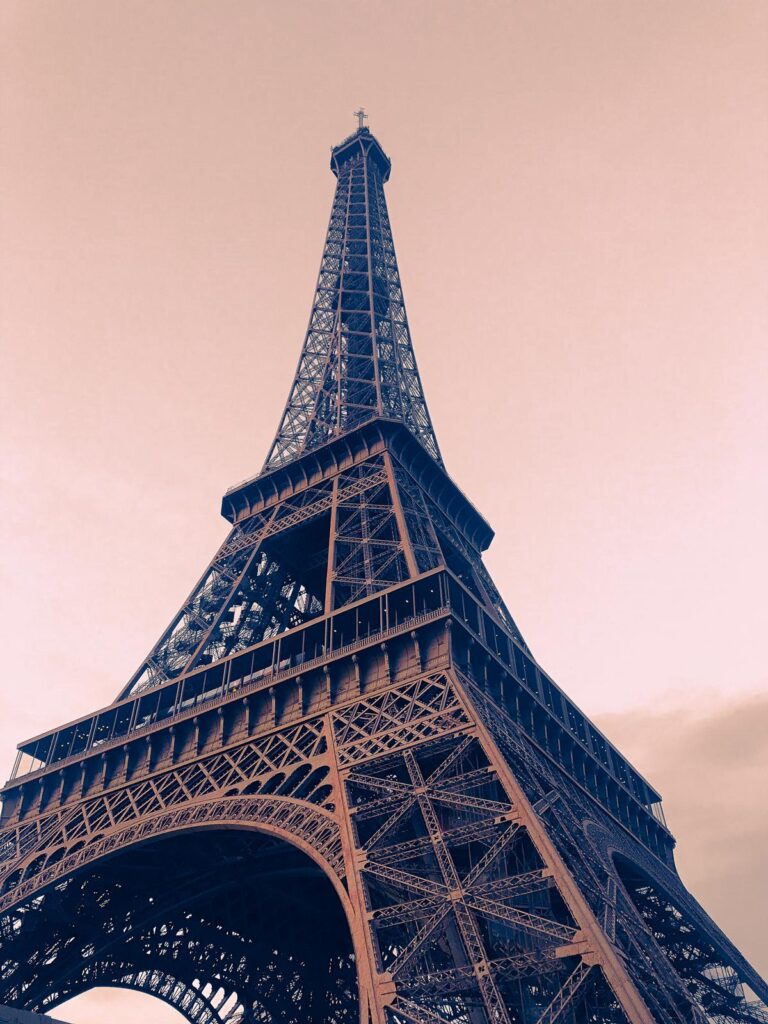 Up-close sepia-toned Eiffel Tower lattice detail against soft sky