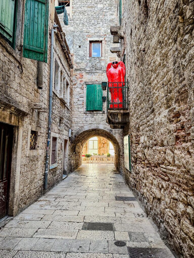 Enchanting Alleyway in Old Town Split, Croatia - Historic cobbled street with green shutters and red sculpture.