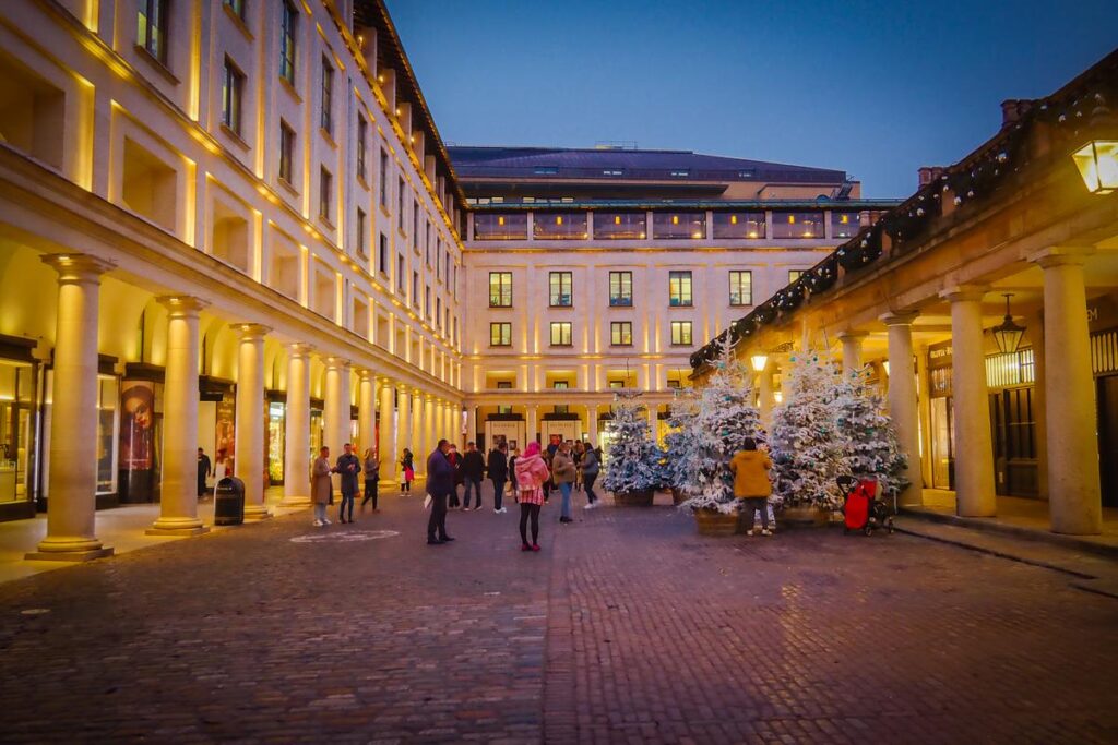 Enchanting Christmas evening at Covent Garden, London, with festive lights, decorations, and shoppers.