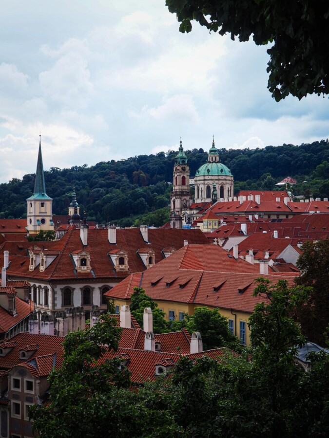Enchanting view of Mala Strana's historic architecture amidst verdant foliage in Prague.