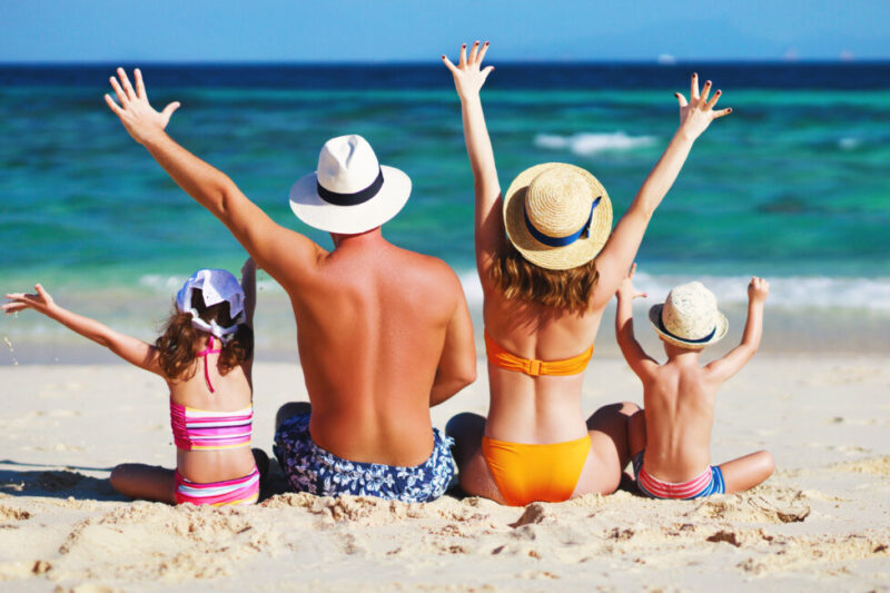 Happy family father, mother and children backs on the beach at sea