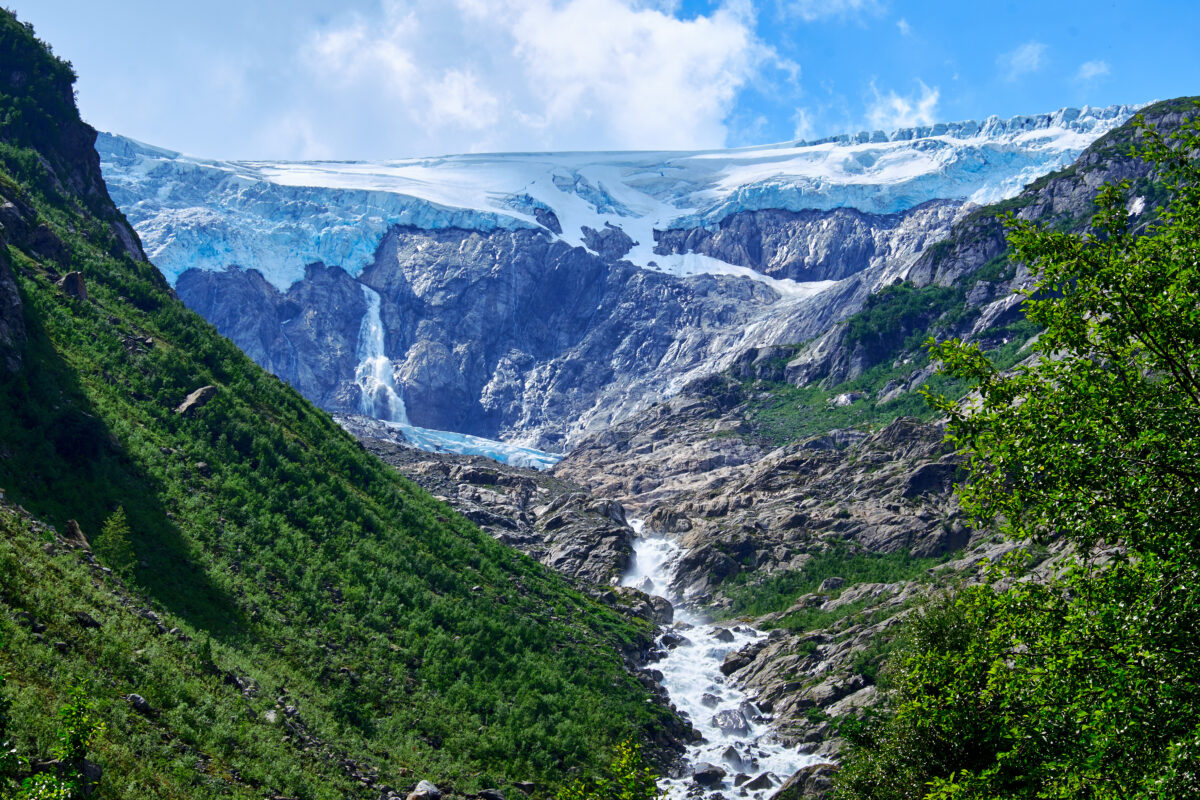 Folgefonna Glacier, Hardanger, Norway, rises over a rugged canyon with ice, waterfalls, and green slopes.