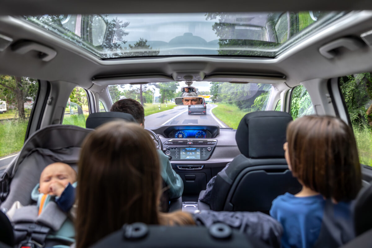 Baby crying in car seat; family road trip; calm siblings, attentive driver on forest road.