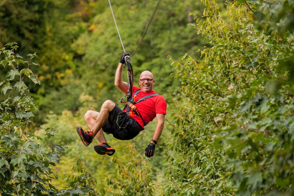 Smiling man enjoying a zip line in Germany through a lush forest.