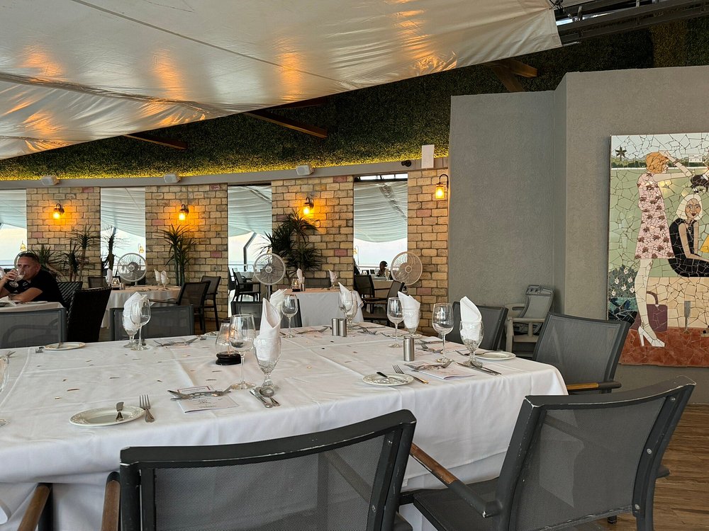 Champers Restaurant Barbados coastal restaurant terrace with white linen table, glassware, canopy, brick columns, and mosaic mural.