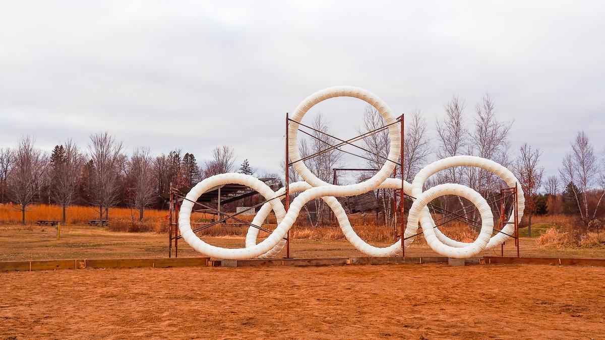 Intertwined white ring sculpture at Franconia Sculpture Park in Minnesota, showcasing modern art in a natural setting under a subdued sky.