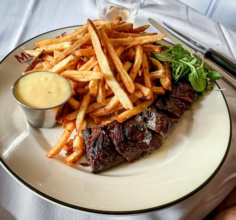 Steak frites with béarnaise sauce on white porcelain plate at French bistro