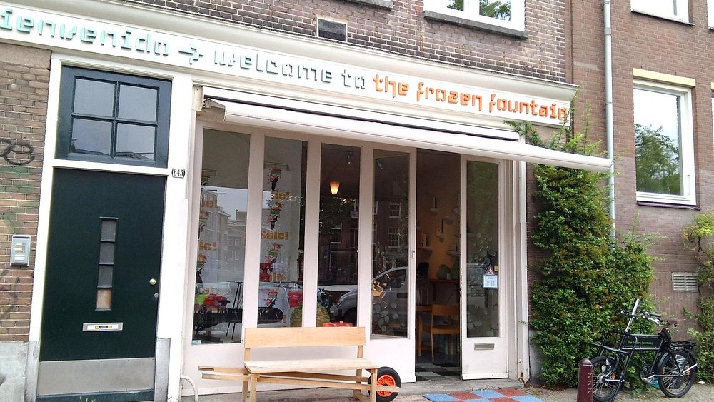 Frozen Fountain storefront among shops in Amsterdam with bicycles and brick facade.