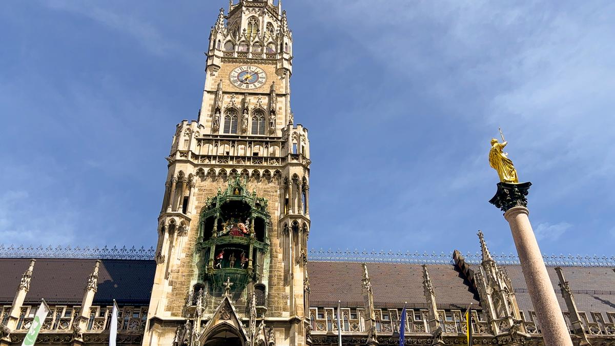 Glockenspiel in Marienplatz, Munich, with neo-gothic New Town Hall tower, vibrant figurines, and Marian column against blue sky