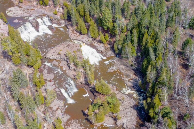 Aerial photograph of Gooseberry Falls with cascading water, evergreen trees, and visitors at the park, illustrating Minnesota's scenic landscapes.