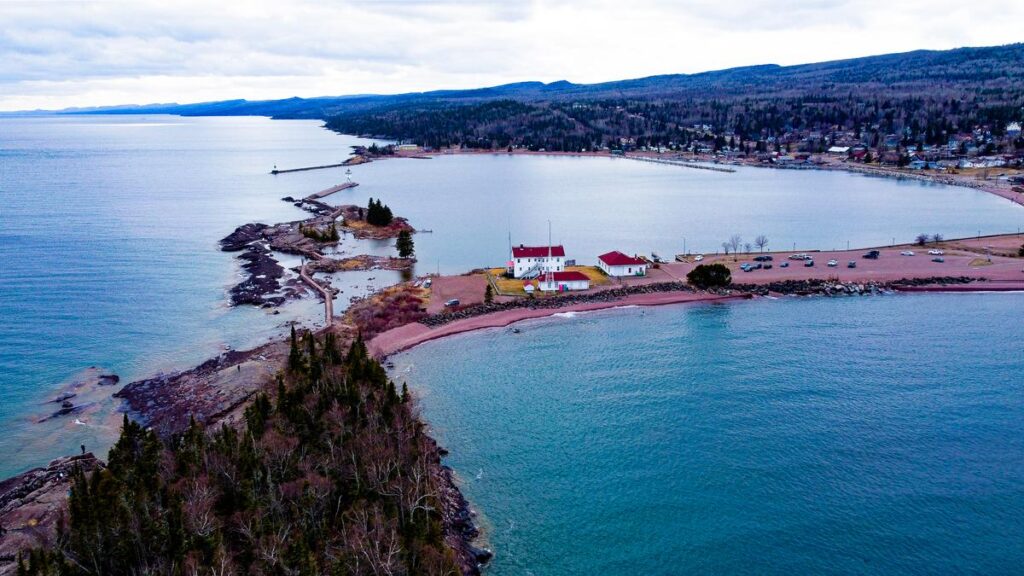 Aerial view of Grand Marais Lighthouse on Artist Point, showcasing hues and serene waters of Lake Superior.
