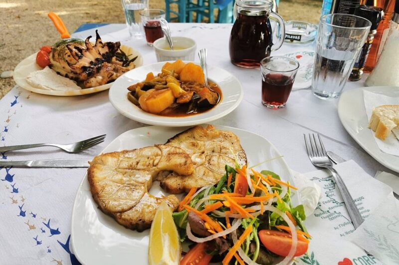 The Fisherman's Cabin Corfu open-air seaside taverna feast: grilled fish steaks, whole grilled seafood, fresh salad, bread basket.