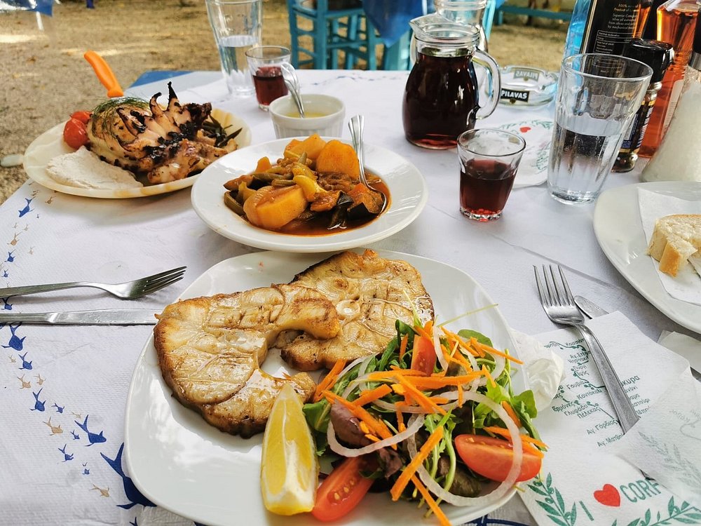 The Fisherman's Cabin Corfu open-air seaside taverna feast: grilled fish steaks, whole grilled seafood, fresh salad, bread basket.