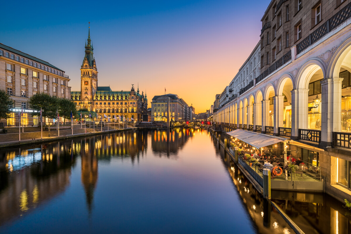 Hamburg City Hall at sunset, iconic landmark reflected on Alster waters.