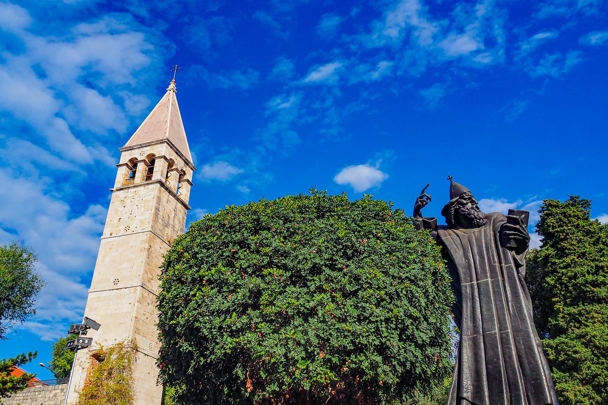 Historic monument of Gregory of Nin statue near church tower in Split, Croatia under clear sky