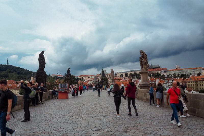 Tourists walking on Charles Bridge with Prague Castle in skyline.