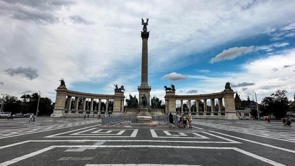 Historic Heroes' Square in Budapest with iconic statues and diverse architecture under a dramatic sky