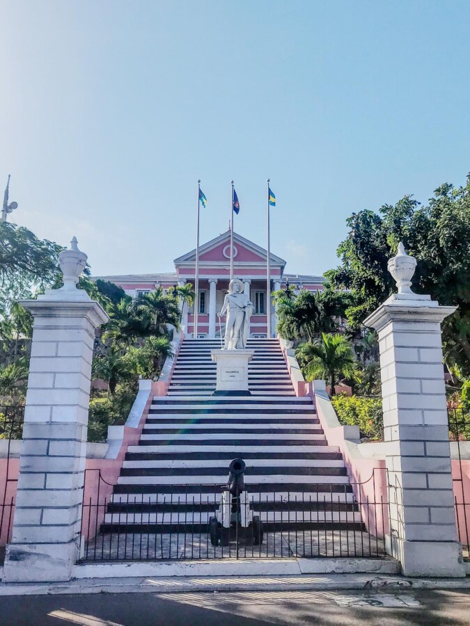 A photo of the Queen's Staircase and pink colonial building with Bahamian flags in Nassau, Bahamas.