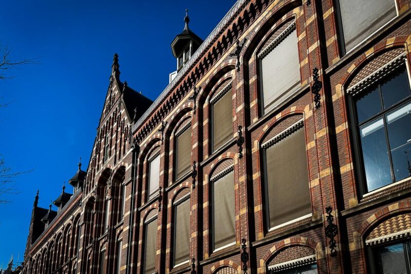 Historic VOC Headquarters Facade in Amsterdam under Blue Sky - Dutch East India Company building with ornate details and iconic gabled rooftops.