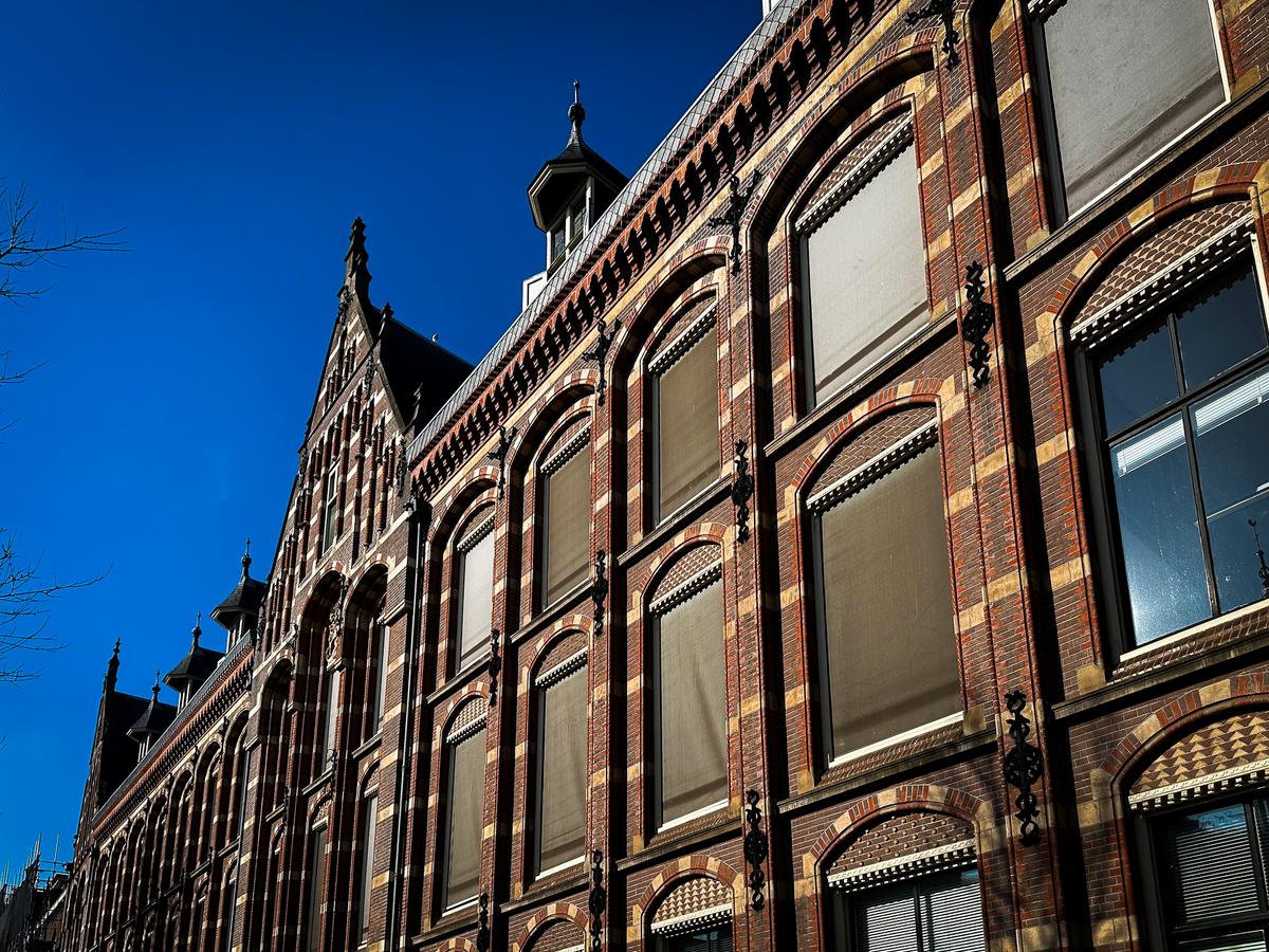 Historic VOC Headquarters Facade in Amsterdam under Blue Sky - Dutch East India Company building with ornate details and iconic gabled rooftops.