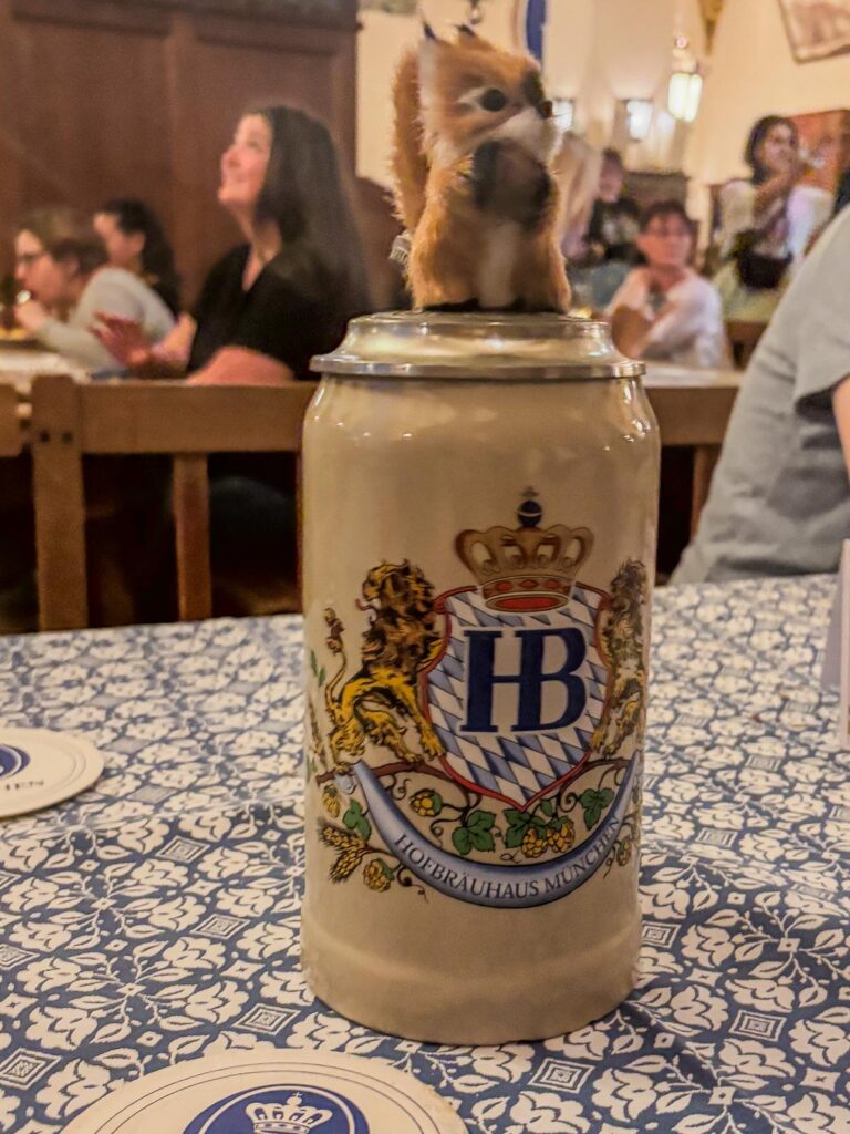 Hofbräuhaus beer hall with patrons, traditional beer stein, and a playful fox toy, Munich nightlife experience.