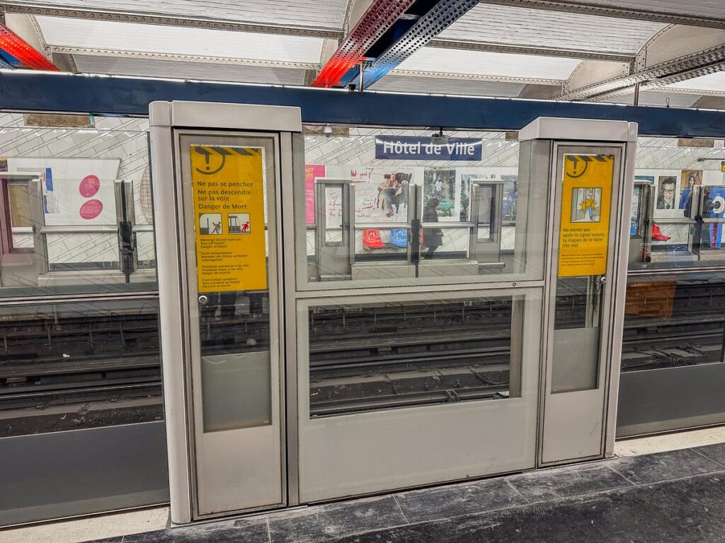 Inside the Hôtel de Ville Metro Station in Paris: Modern platform with safety signage and passengers.