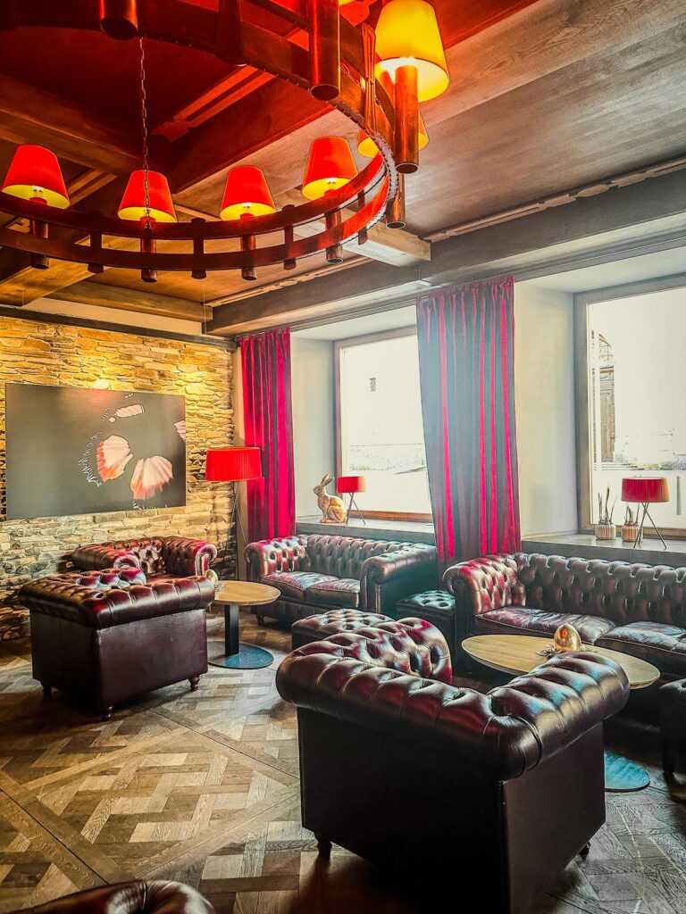 Elegant Hotel Grauer Bär lobby with Chesterfield sofas, red curtains, rustic chandelier, and herringbone flooring.