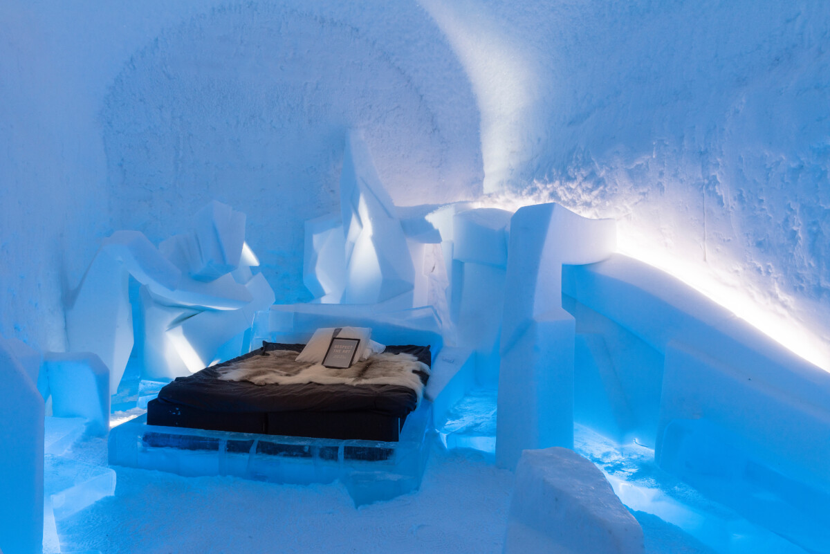 Sculpted ice room with a bed and carved wall details at ICEHOTEL