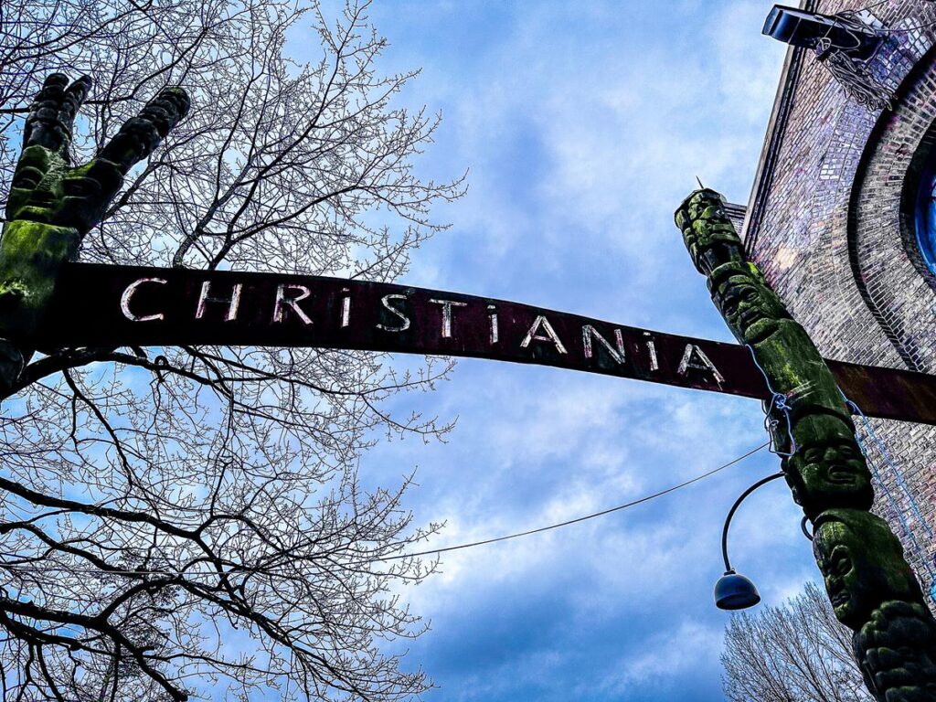 Christiania entrance sign and sculpture beneath a blue sky