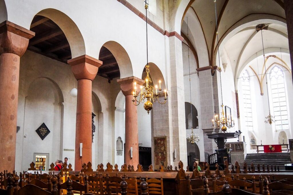Interior of Pieterskerk Utrecht showcasing Romanesque columns, Gothic arches, wooden pews, and majestic chandeliers