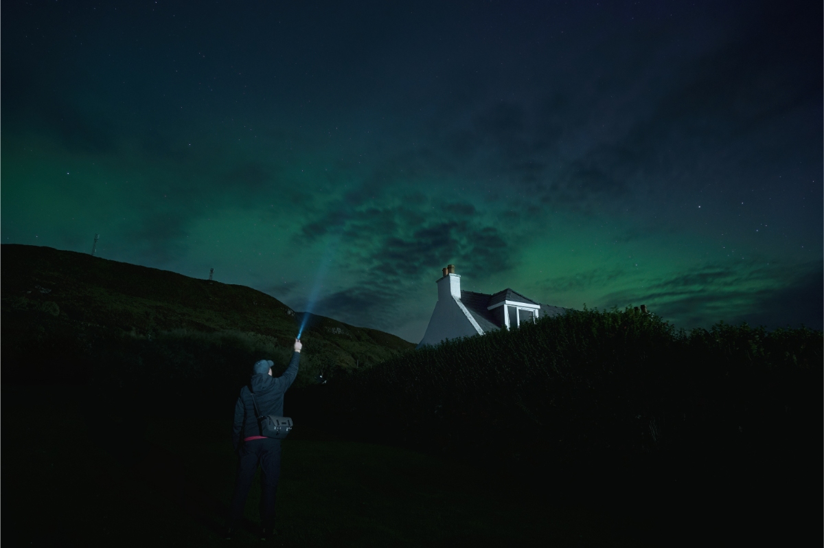 Man looking at the Northern lights over the Isle of Skye, Scotland