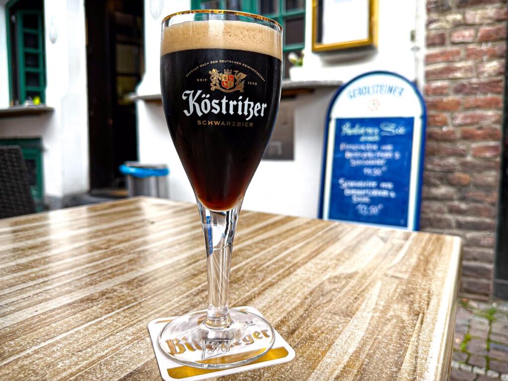 High-res image of impeccably poured Köstritzer Schwarzbier in branded glass at authentic outdoor European bistro