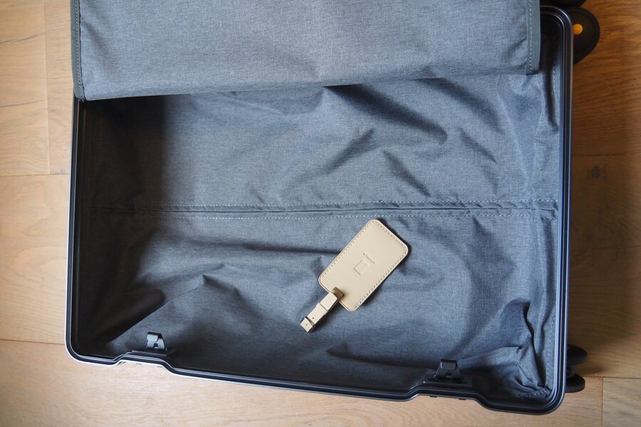 An empty aluminum carry-on compartment shows grey lining, stitched seams and a hanging luggage tag.
