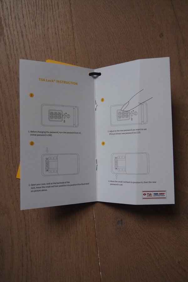 Printed TSA lock instructions show the combination dials and reset mechanism for the aluminum carry-on.